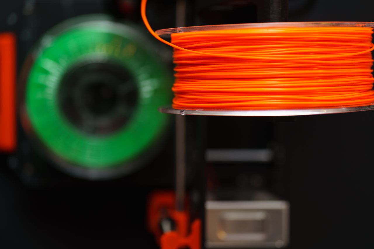 services-03 Detailed view of orange and green 3D printer filament spools, perfect for creative and industrial projects.
